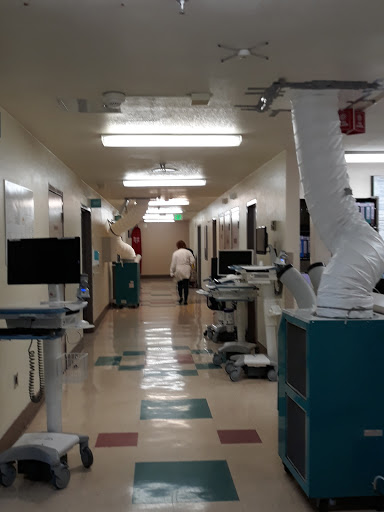A view of a hospital hallway with medical equipment and a healthcare professional walking in the distance.