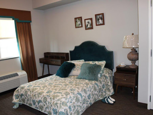 A cozy bedroom featuring a floral-patterned bedspread, plush pillows, and decorative photos on the wall.