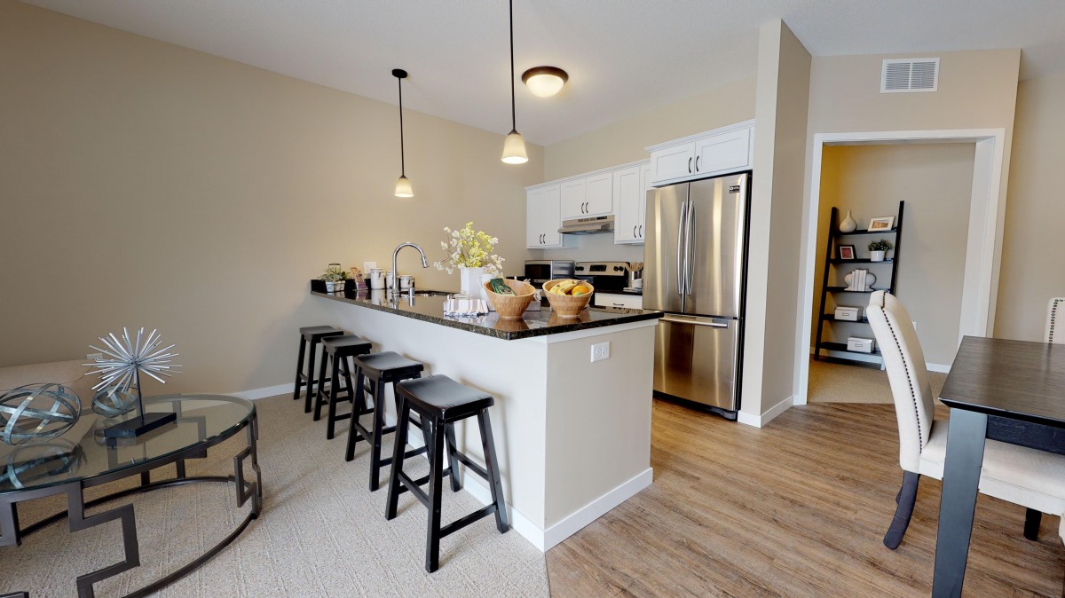 A modern kitchen with an island and stainless steel appliances, featuring pendant lights and bar stools.