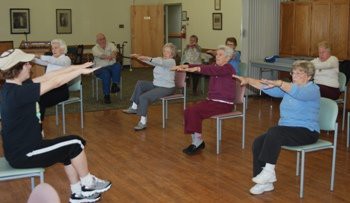 A group of seniors participating in a seated exercise class indoors.