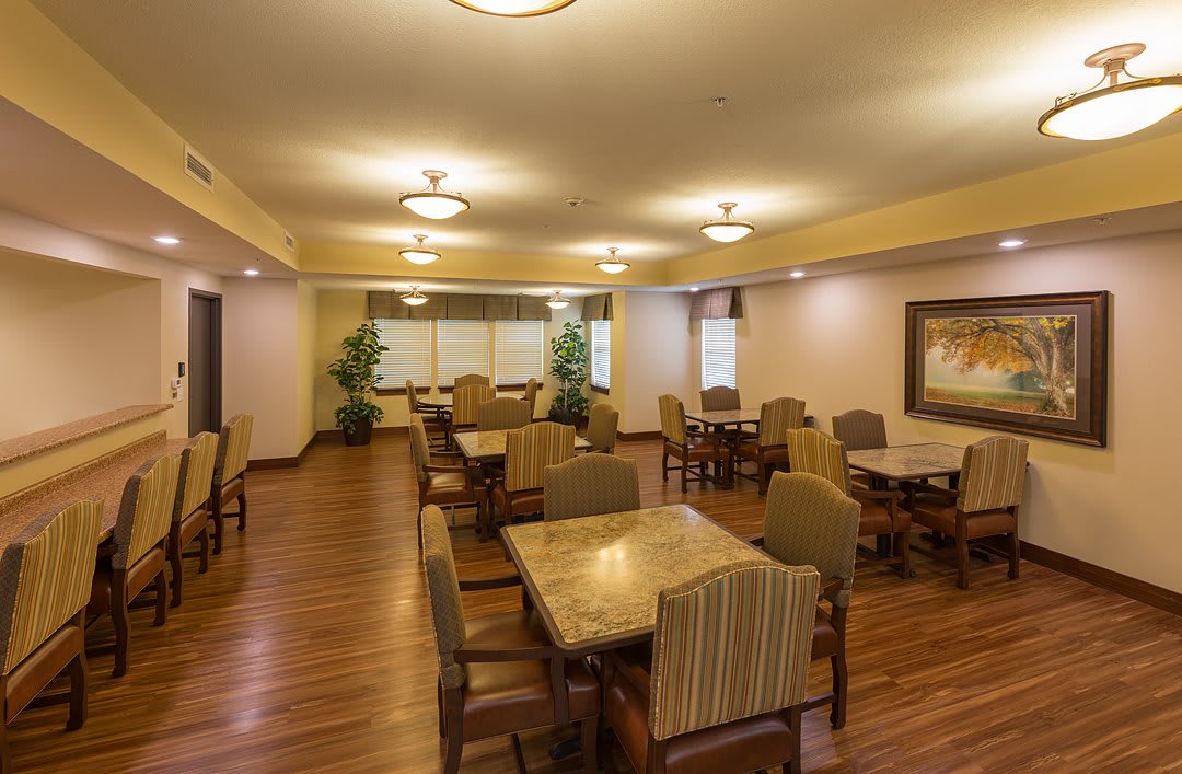 A dining area with neatly arranged tables and chairs, featuring warm lighting and wooden floors.