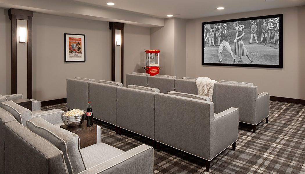 A cozy home theater setup with gray seating, a classic popcorn machine, and a movie playing on the screen.
