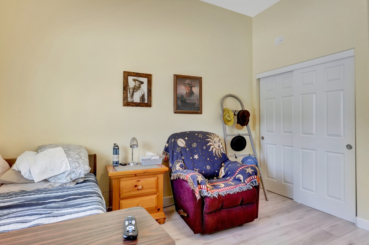 A cozy bedroom featuring a colorful armchair, nightstand with a lamp, and decorative paintings on the wall.