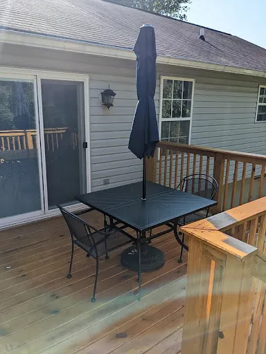 A cozy outdoor dining setup on a wooden deck with a table, chairs, and an umbrella.