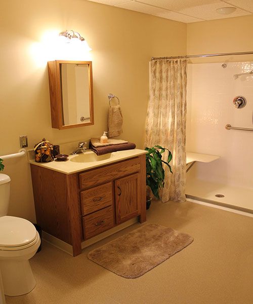 A clean and cozy bathroom featuring a wooden vanity, mirror, toilet, and walk-in shower.