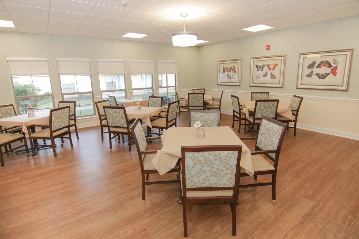 A neatly arranged dining room with multiple tables and chairs, featuring soft lighting and large windows.