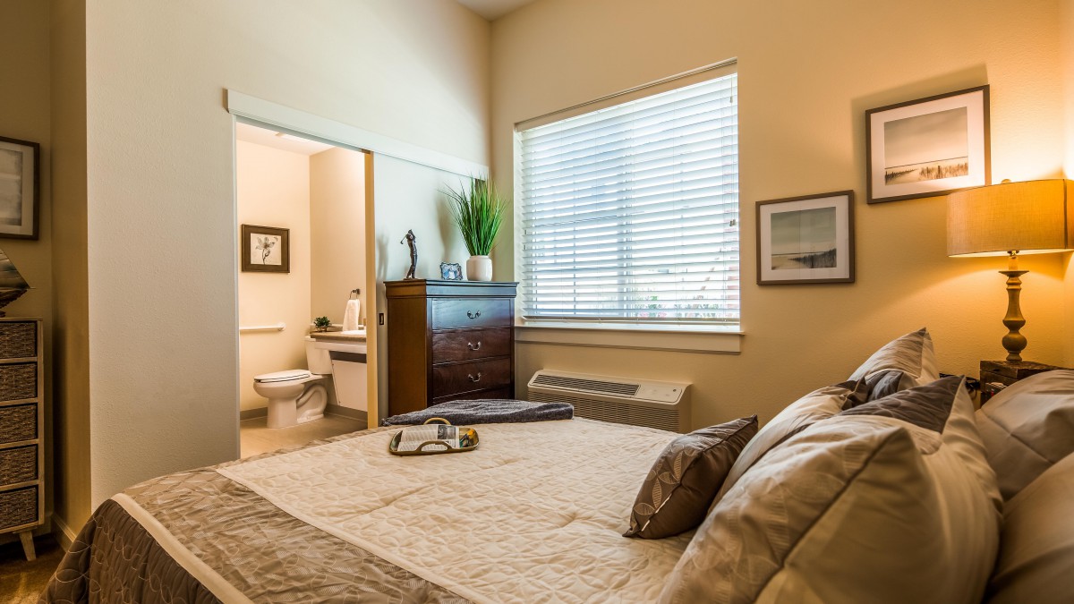 A cozy and well-lit bedroom featuring a neatly made bed, a window with blinds, and tasteful decor.