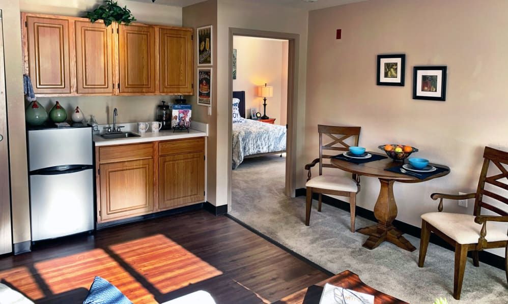 A cozy apartment interior featuring a compact kitchen, dining table, and a glimpse into the bedroom.