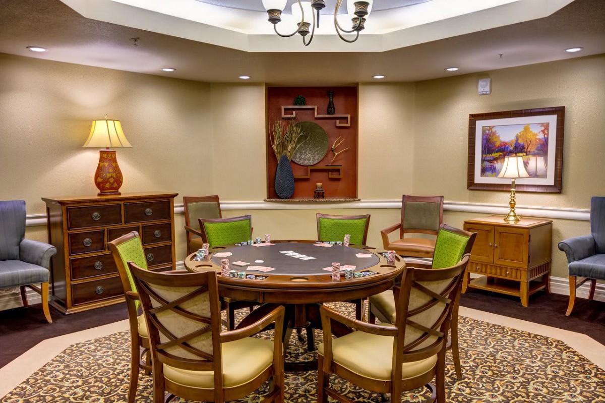 A cozy game room with a round poker table surrounded by wooden chairs, elegant lighting, and tasteful decor.