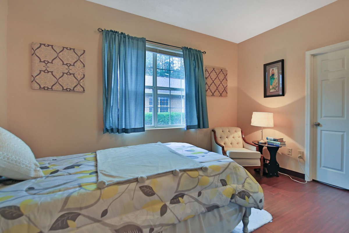 A cozy bedroom with a bed, chair, and lamp near a window.
