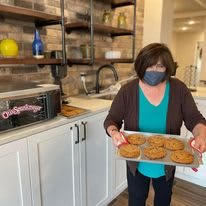 A person wearing a mask holds a tray of freshly baked cookies in a kitchen.