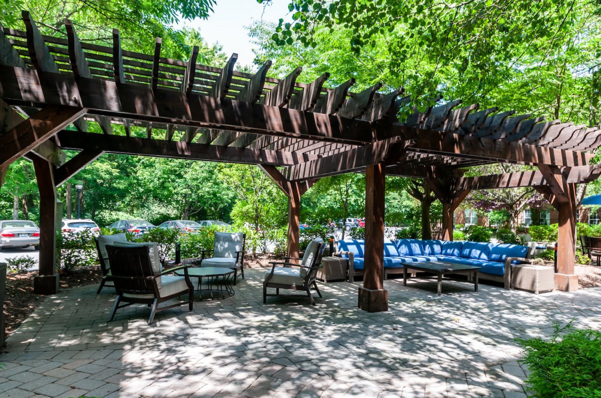 A shaded outdoor seating area with a pergola and comfortable furniture surrounded by lush greenery.