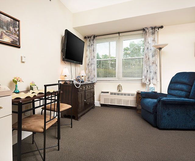 A cozy living room with a TV, chair, and a dining table near the window.