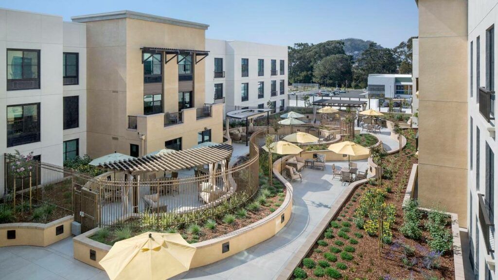 A modern building with a landscaped outdoor area featuring walkways and umbrellas.