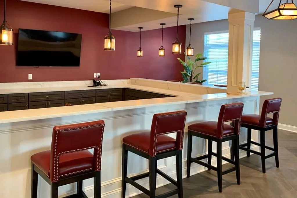 A modern bar area with red stools and pendant lighting.