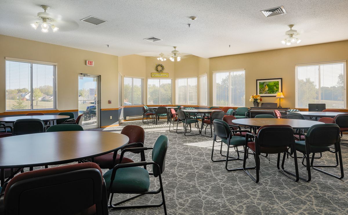 A well-lit conference room with round tables and chairs, featuring large windows and a carpeted floor.