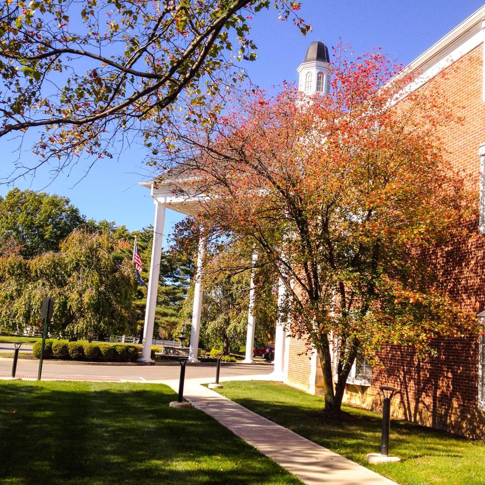 A brick building with white columns surrounded by autumn trees and a sidewalk.