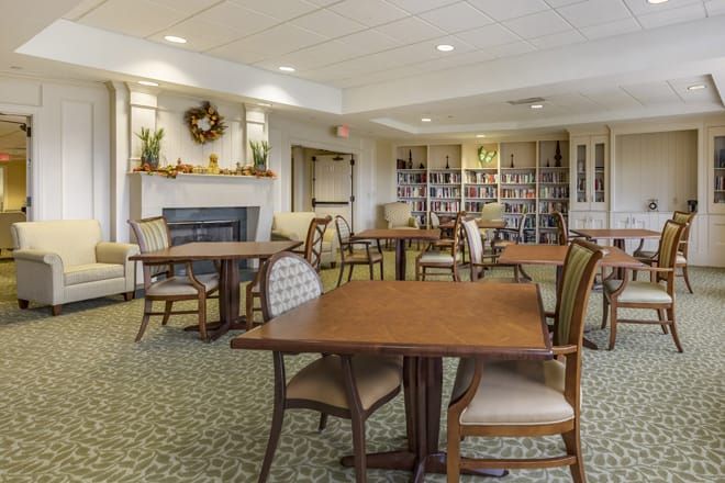 A cozy dining area with tables, chairs, a fireplace, and a bookshelf.
