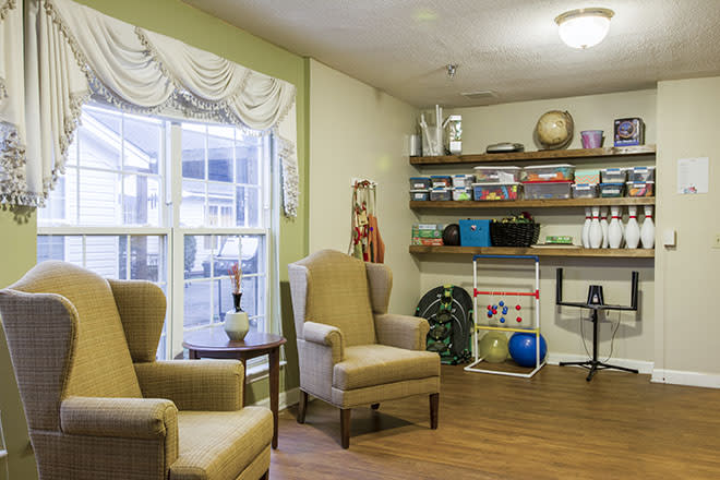 A cozy living room with armchairs, bookshelves, and a large window providing natural light.
