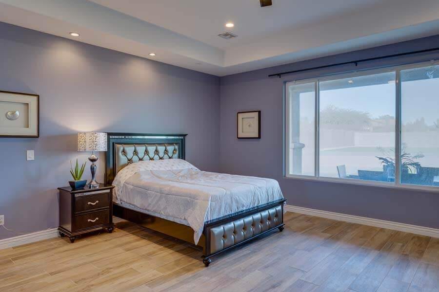 A modern bedroom with a blue color scheme, featuring a bed, nightstand, and large window.