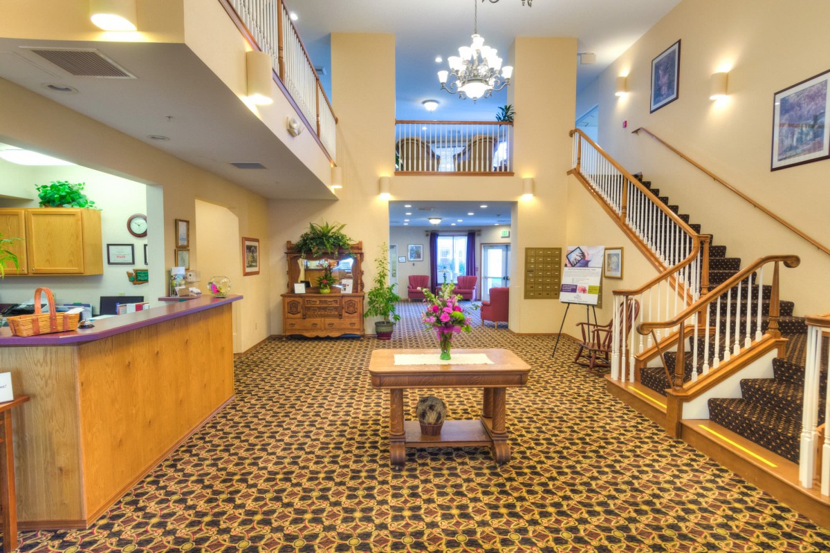 A spacious hotel lobby with a reception desk, central decorative table, and chandelier lighting.