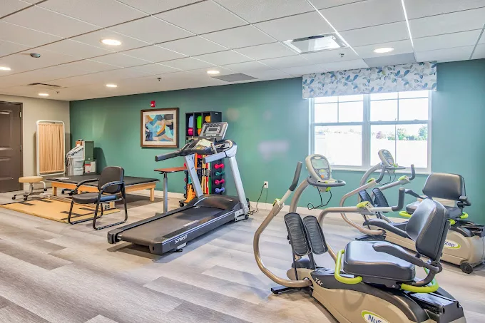 A well-lit indoor gym featuring exercise equipment including a treadmill and stationary bikes.