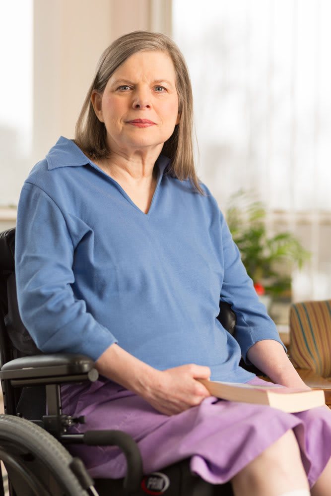 A woman in a blue shirt sitting indoors holding a book.