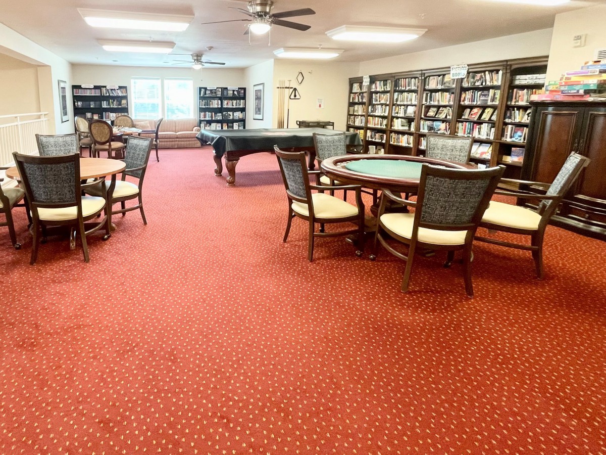 A spacious library reading area with bookshelves, tables, chairs, and a pool table.