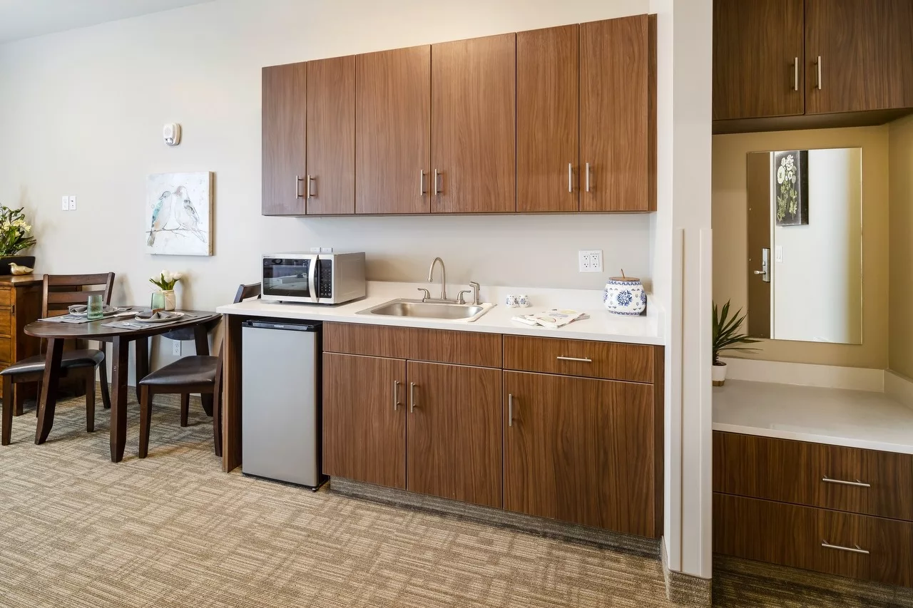 A modern kitchenette with wooden cabinets, a stainless steel refrigerator, and a microwave.