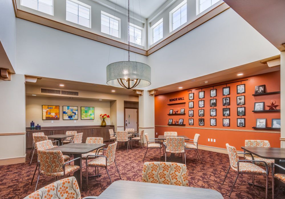 A modern dining area with a high ceiling, featuring multiple seating arrangements and decorative artwork on the walls.
