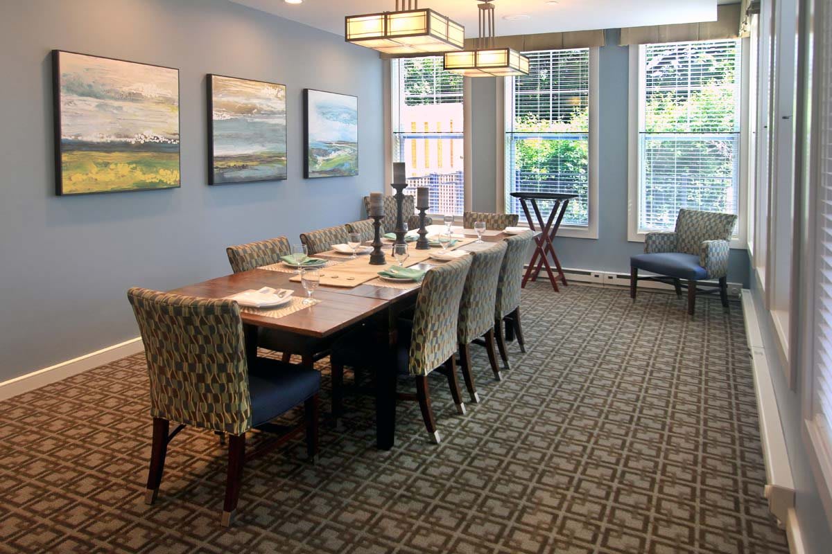 A well-decorated dining room with a large table and chairs, featuring artwork on the walls and ample natural light from the windows.