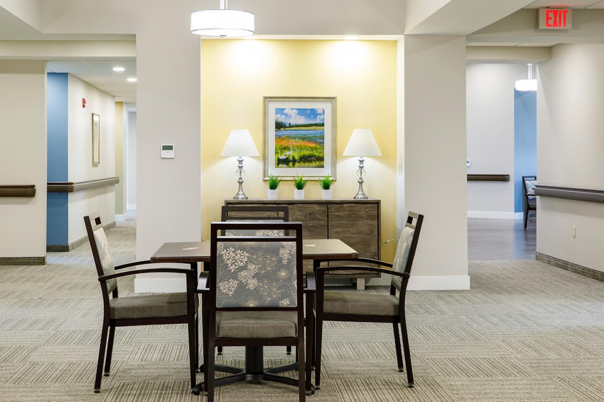 A well-lit room with a table and four chairs, featuring wall art and two lamps on a sideboard.