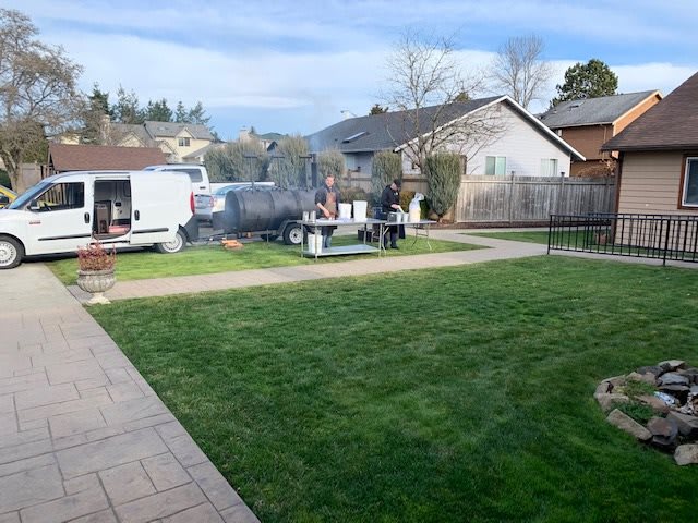 A backyard scene with green grass, neighboring houses, and a patio area.
