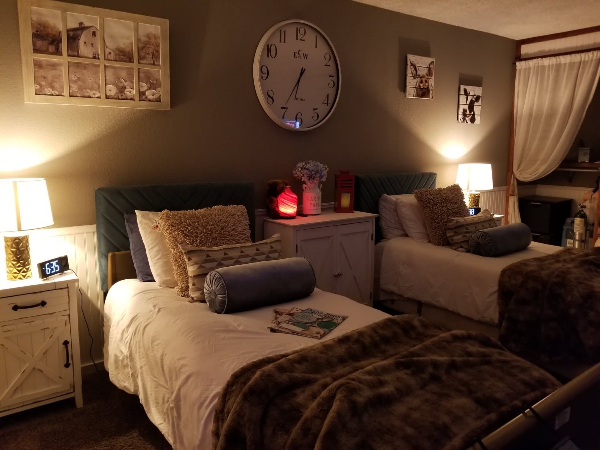 A cozy bedroom with twin beds softly lit by lamps, adorned with plush pillows and blankets.