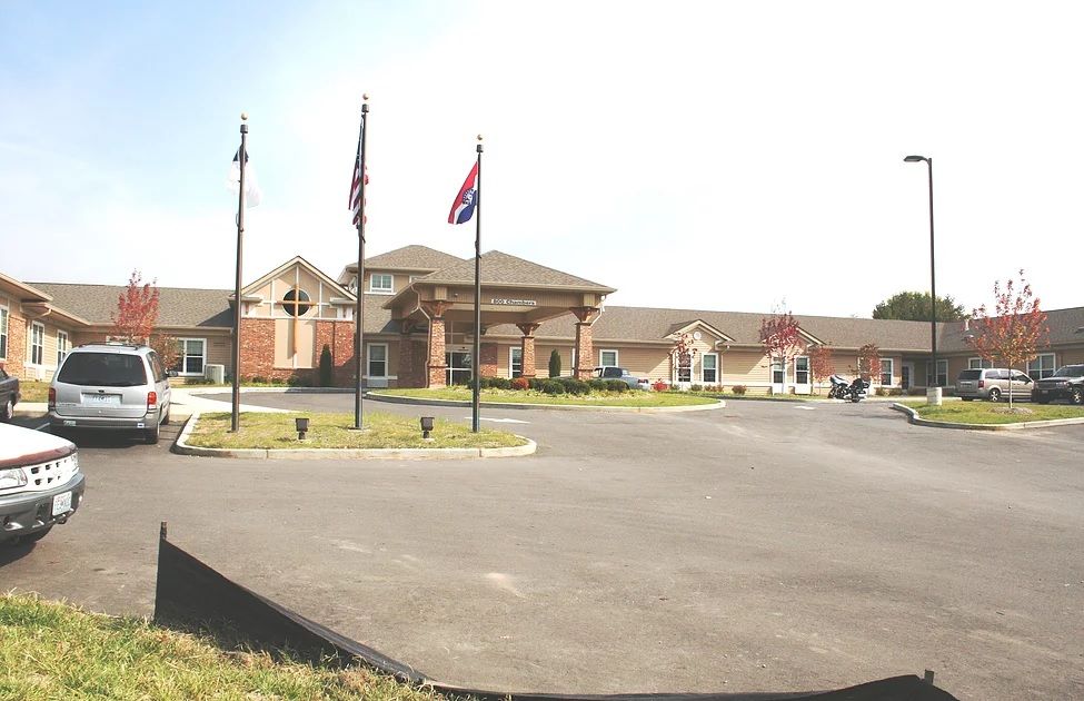 A single-story building with multiple flags in front, surrounded by a parking lot under clear skies.