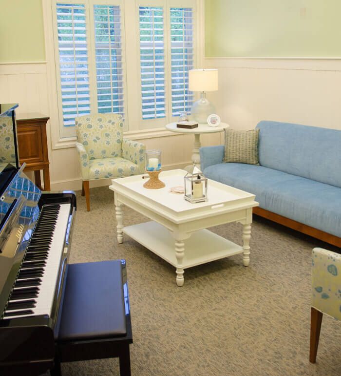 A cozy living room featuring a blue sofa, a white coffee table, and a piano by the window.