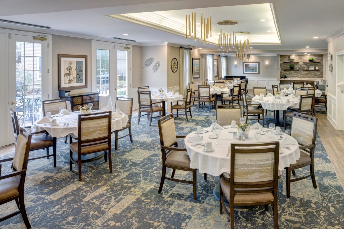 An elegant dining room with neatly arranged tables and chairs, featuring chandeliers and tasteful decor.