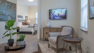A cozy living space featuring a comfortable chair, a wall-mounted TV, and a stylish transition into the bedroom.