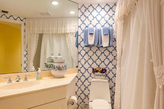A cozy bathroom with patterned wallpaper, neatly arranged towels, and a well-lit vanity area.
