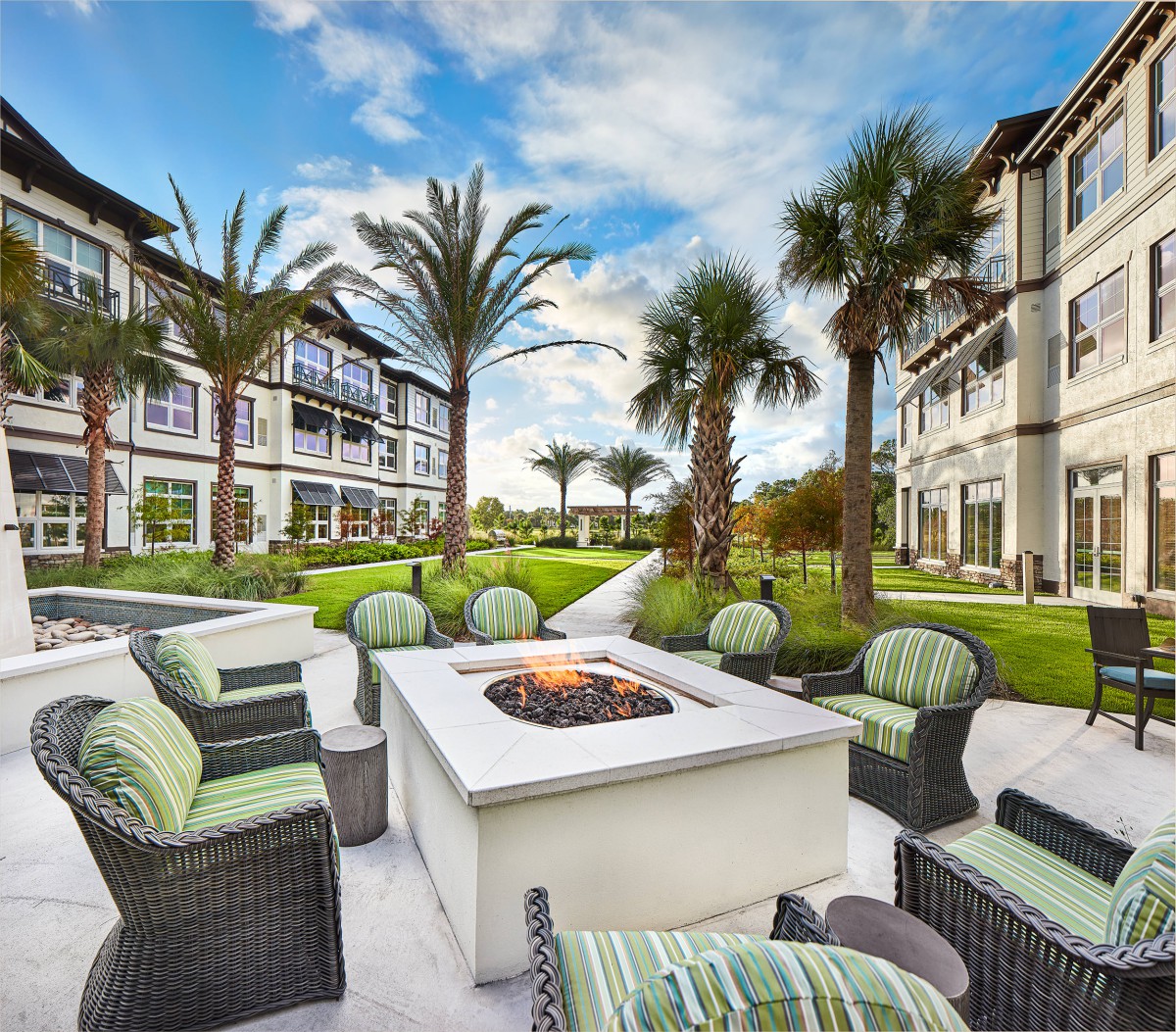 A modern residential complex features a cozy outdoor seating area with a fire pit surrounded by palm trees.