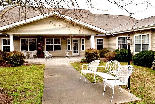 A charming house with outdoor seating on a patio, surrounded by landscaped greenery.