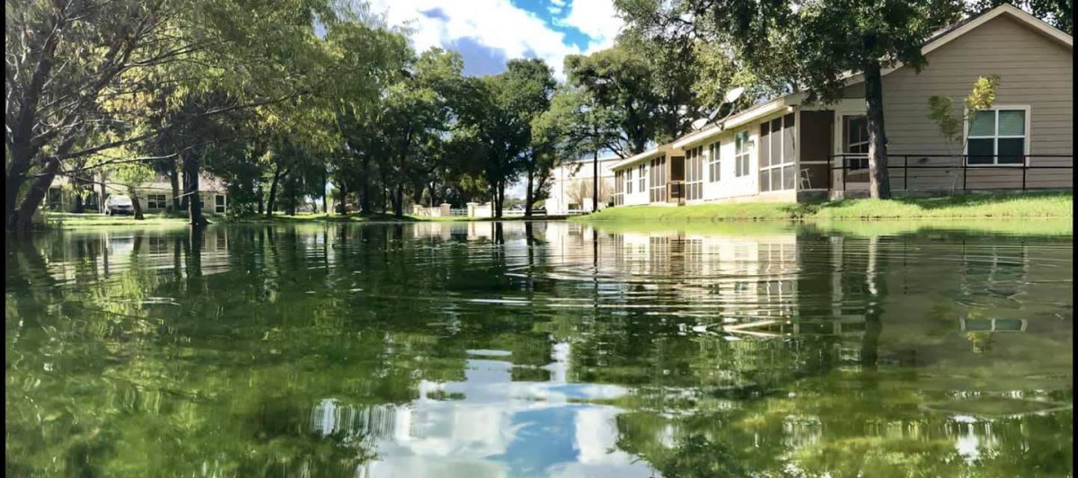 A tranquil view of a lake reflecting the sky and surrounding trees, with a building on the shore.