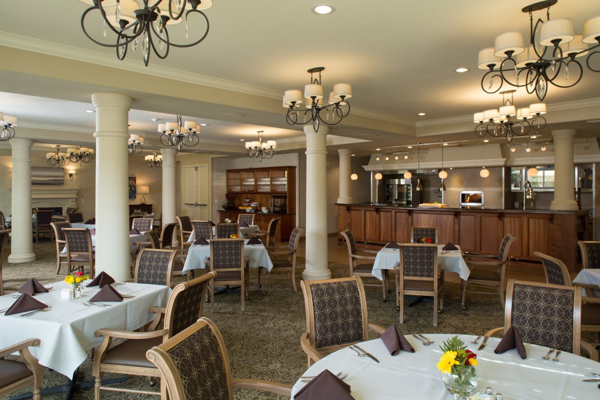 A cozy restaurant dining room with elegant chandeliers and a bar area.