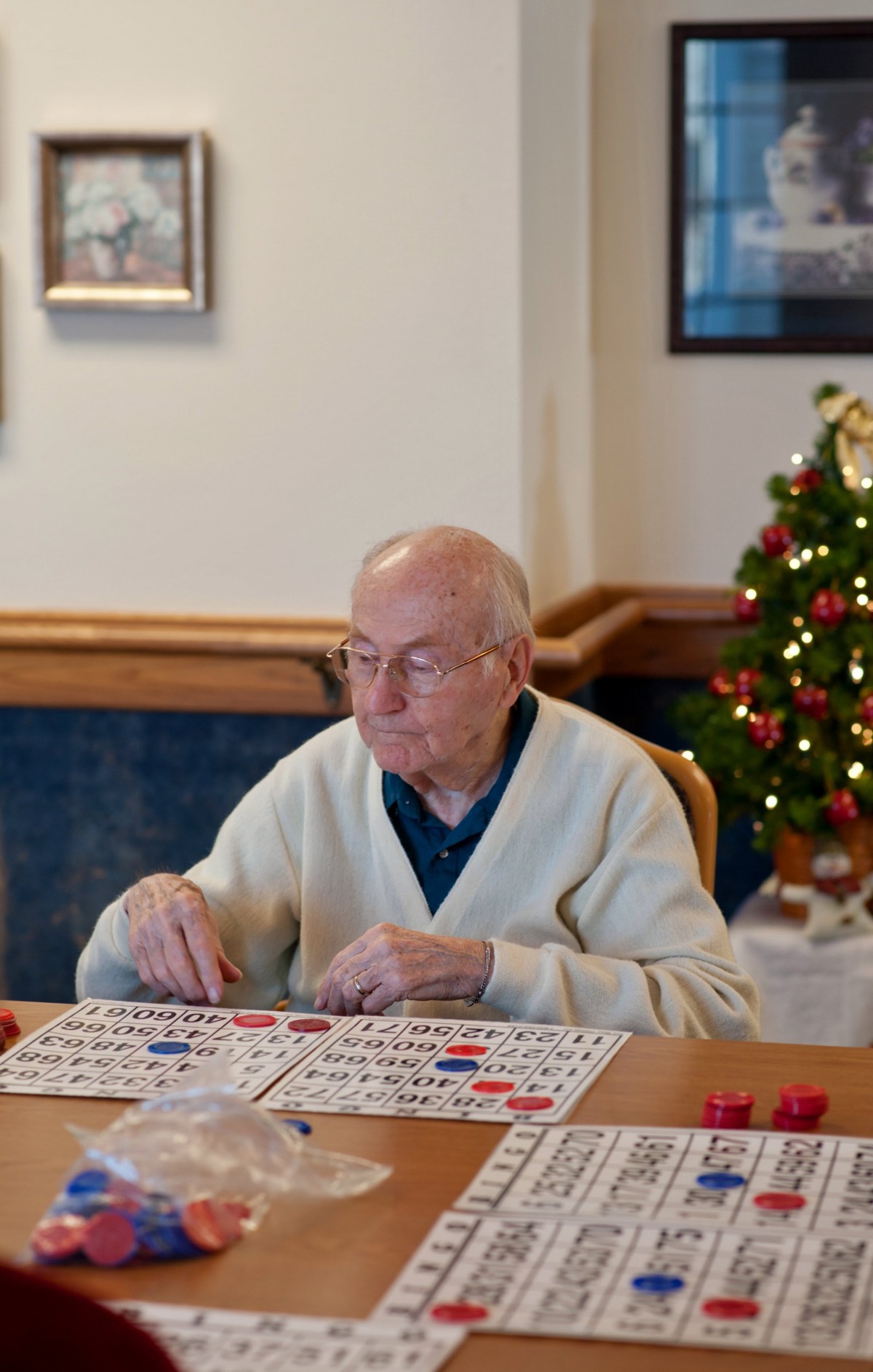 An elderly man playing bingo indoors, surrounded by festive Christmas decorations.
