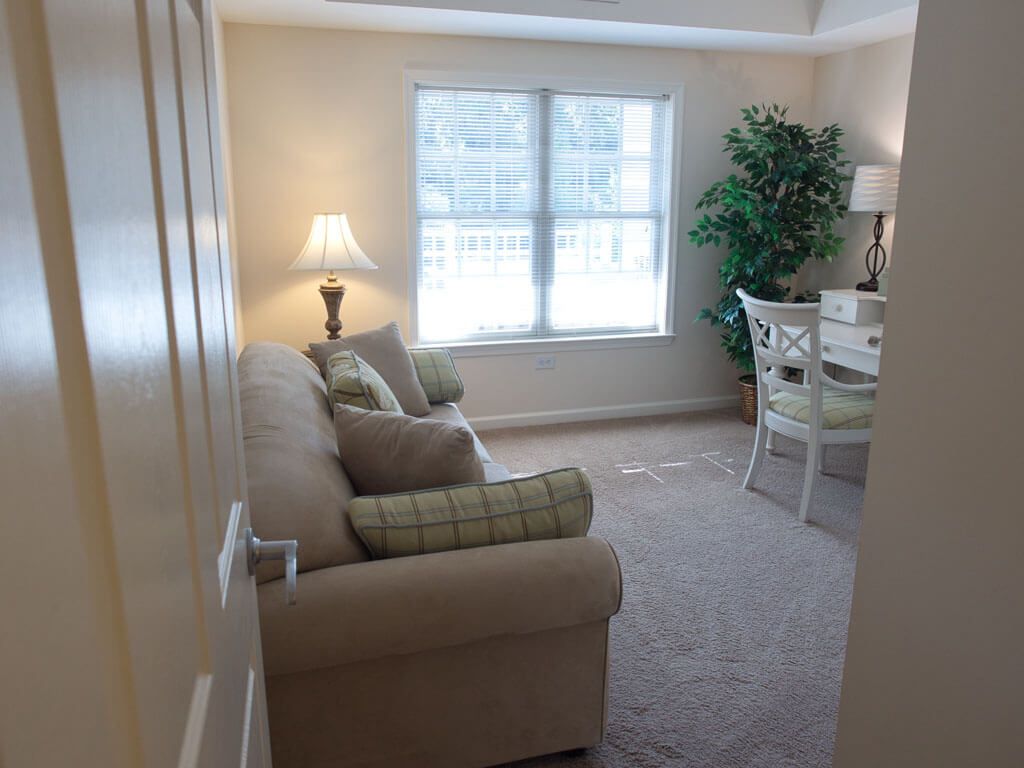 A cozy living room with a sofa, desk, and potted plant by the window.