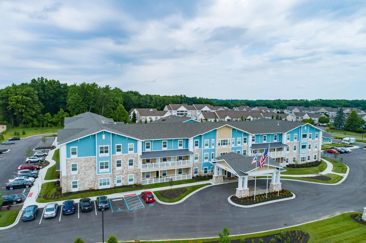 Aerial view of a blue residential apartment complex with surrounding greenery and parking area.