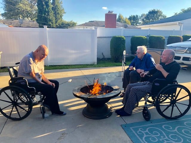 Elderly individuals enjoying a sunny day around a fire pit in wheelchairs.