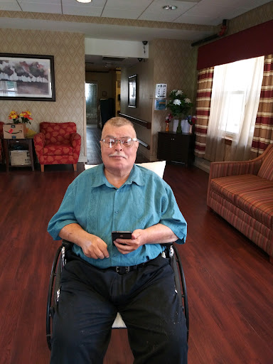 An elderly person seated in a wheelchair holding a smartphone, surrounded by a cozy living space.