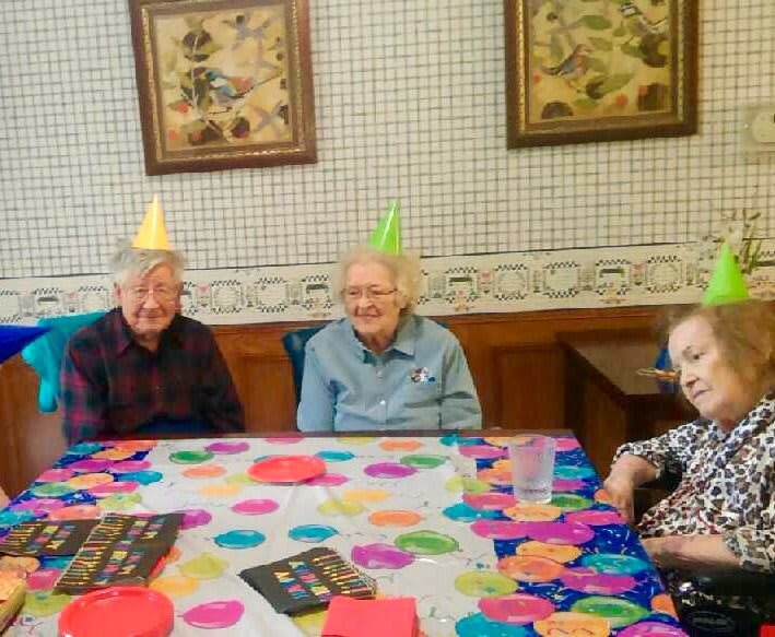 Elderly individuals celebrating a birthday with party hats and decorations.