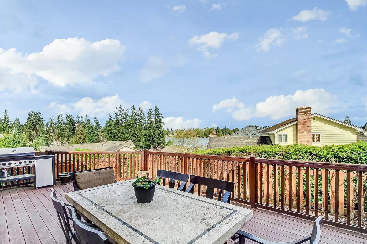 A spacious outdoor deck with a table and chairs, surrounded by trees under a clear blue sky.